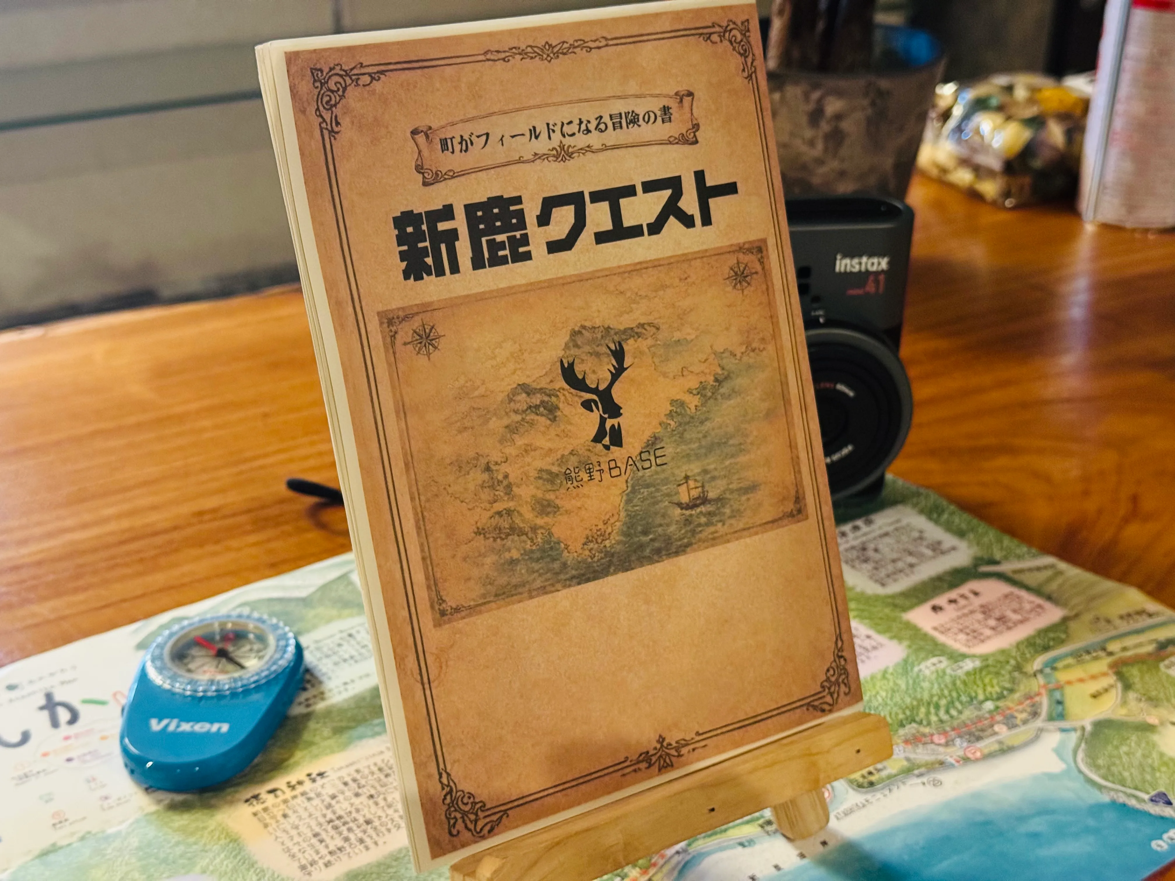 「新鹿クエスト」冊子とコンパス、手書きMAPをテーブルに立てて展示